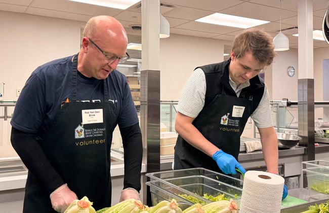 Two FEG volunteers in Ronald McDonald House Charities aprons preparing lettuce in a commercial kitchen during a community service event.