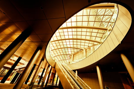 Claude responded: Dramatic upward view of a modern atrium with a circular glass skylight, curved balconies, and an escalator bathed in golden light.Dramatic upward view of a modern atrium with a circular glass skylight, curved balconies, and an escalator bathed in golden light.