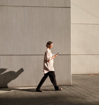Woman walking past a corrugated metal wall, checking her phone in warm afternoon light.